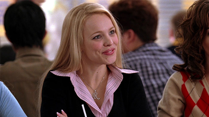 Person at a table with long blonde hair, wearing a pink blouse, discussing petty grudges.