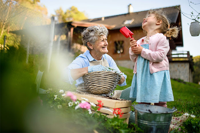 Grandmother and child gardening together, sharing joyful moments near a house, surrounded by flowers and garden tools.