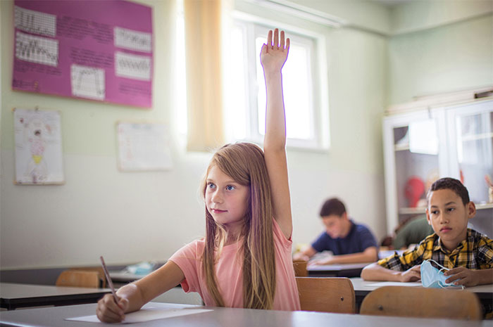 A young student raises her hand in a classroom, eager to participate in the lesson.