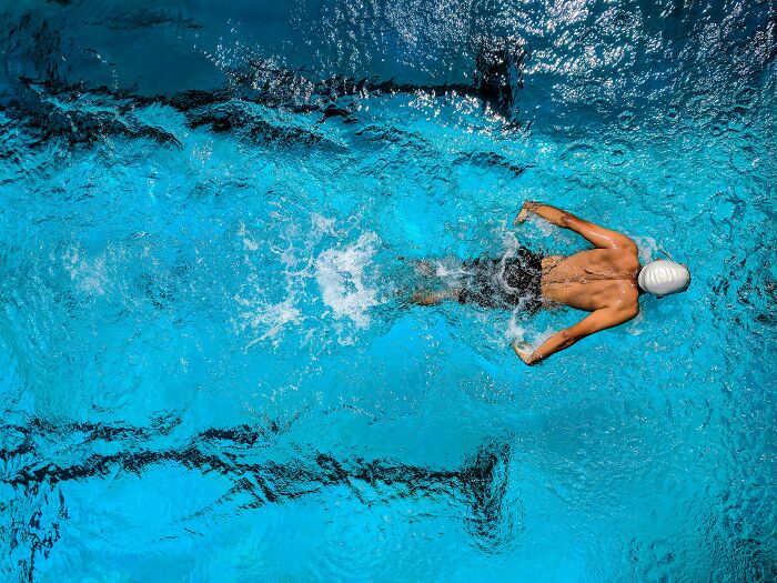 Swimmer in a pool, wearing a swim cap, gliding through water, unrelated to rumors being spread.