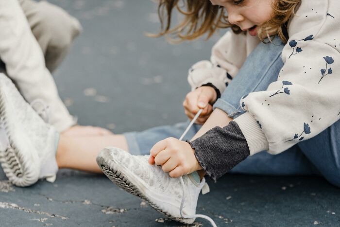 Child tying shoelaces outdoors, wearing a patterned sweater, capturing a candid moment of focus and humor in overheard conversations.