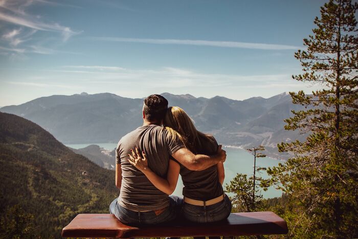 Couple on a bench overlooking a scenic mountain view, sharing an eye-opening moment.