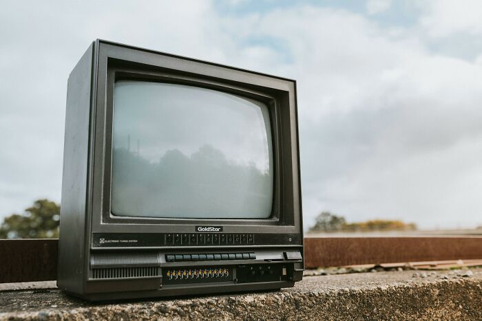 An old television set on a concrete ledge under a cloudy sky, highlighting outdated future predictions.