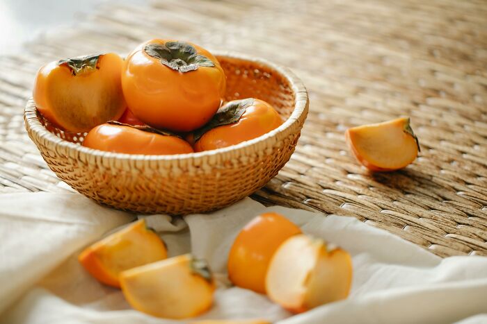 Basket of persimmons on a woven surface, representing health-boosting fruits for your fridge.
