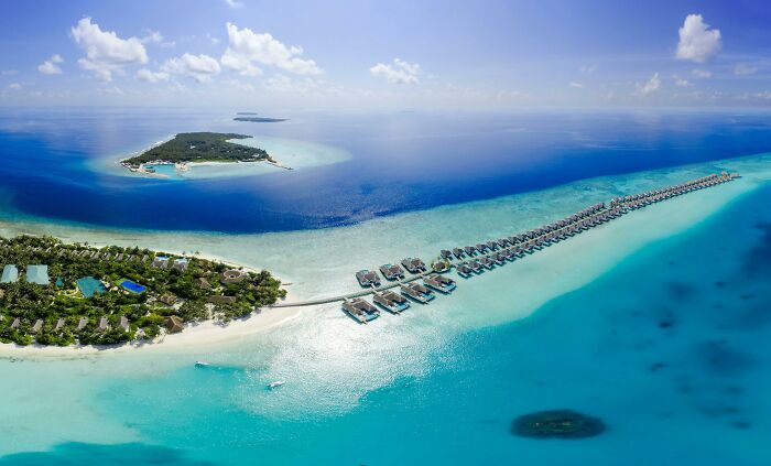 Aerial view of a stunning natural wonder, featuring clear blue waters and a tropical island with overwater bungalows.