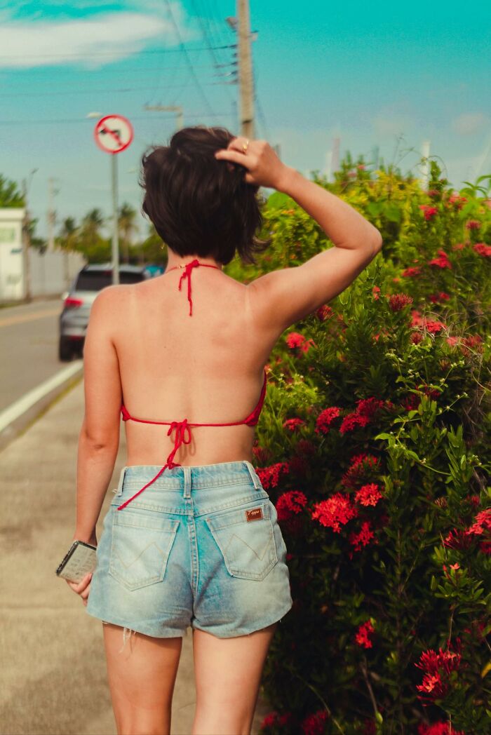 Person in shorts and bikini top walks past red flowers, highlighting culture shocks in different countries.