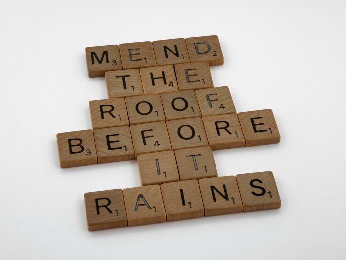 Scrabble tiles spelling out the idiom "Mend the roof before it rains" on a white background.