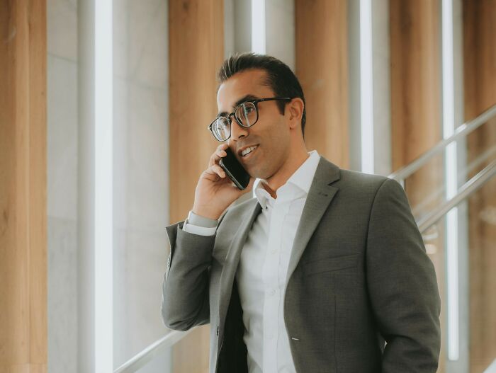 Man in a suit on phone, smiling beside modern staircase, illustrating harsh realities about life in a business setting.