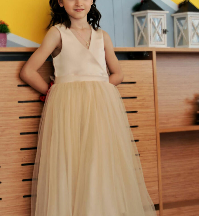 Child in a cream dress, leaning against a wooden cabinet, with decorative lanterns in the background.