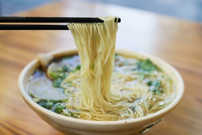 Chopsticks lifting noodles from a bowl of soup, highlighting cultural differences in dining practices.