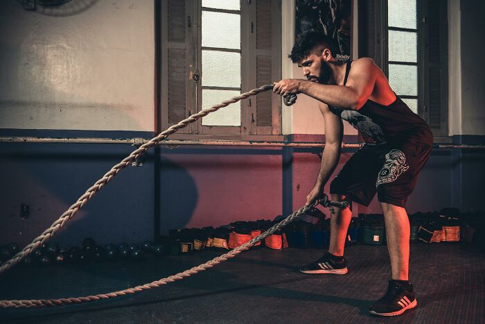 Man exercising with battle ropes in an indoor gym, showcasing fitness equipment often associated with rich people.