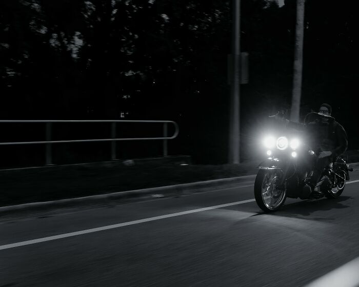 Motorcycle rider on a dimly lit road at night, an eye-opening moment captured with bright headlights illuminating the path.