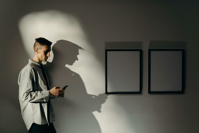 Person holding a phone, casting a shadow on an office wall with empty frames, capturing an office humor moment.