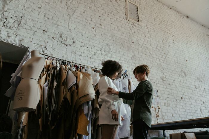 Fashion designer fitting a white blazer on a model in a studio, illustrating things associated only with rich people