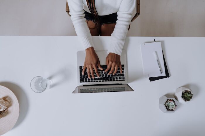 Person typing on a laptop, symbolizing professions that might be useless soon, with a notebook and succulents on a desk.