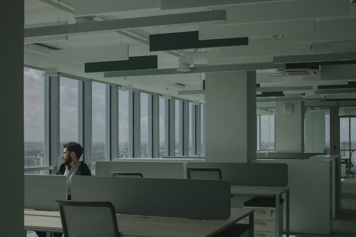 Man in an office with empty cubicles, looking out large windows, contemplating revenge on someone in power.