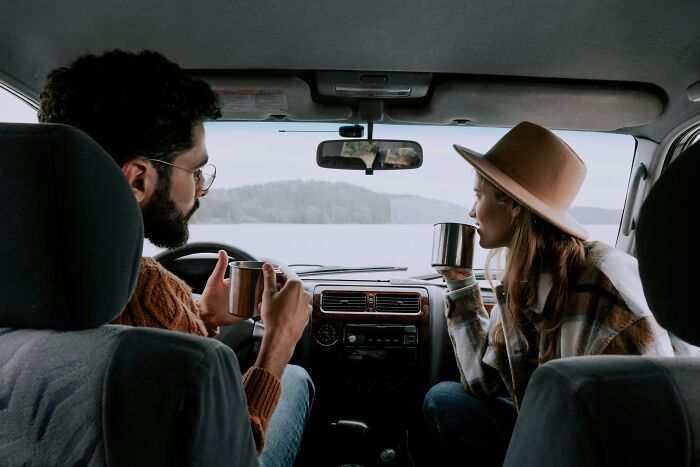 Couple enjoying coffee in a car, sharing a moment of love by the lake.