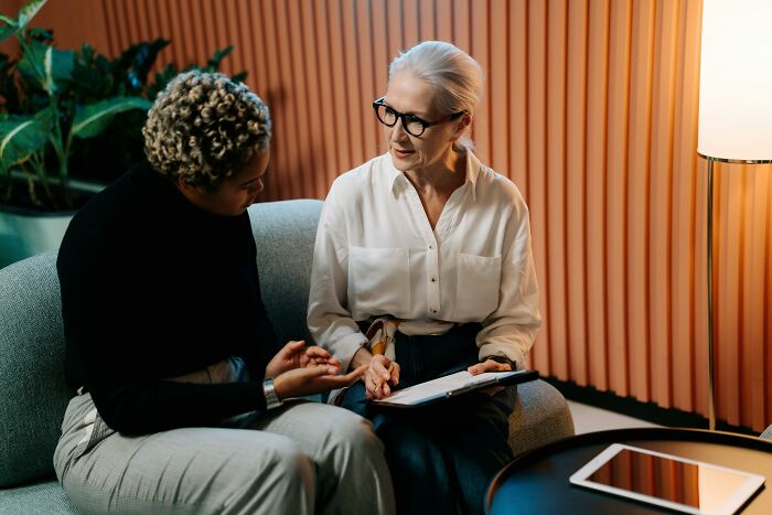 Two women in discussion on a couch, one holding a tablet, symbolizing often overlooked professions.