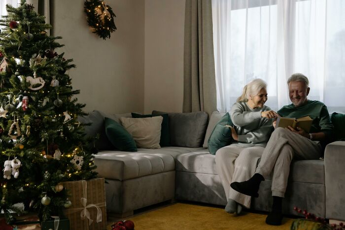 Elderly couple sharing eye-opening moments on a cozy sofa near a decorated Christmas tree.