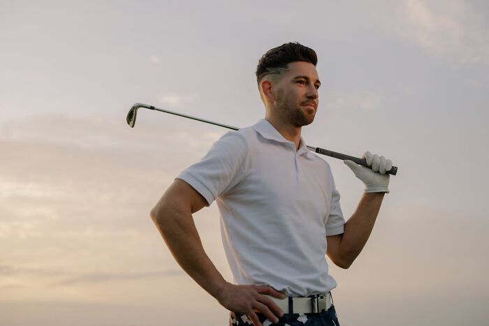 Man in a white polo shirt holding a golf club, representing revenge on authority in a serene landscape.
