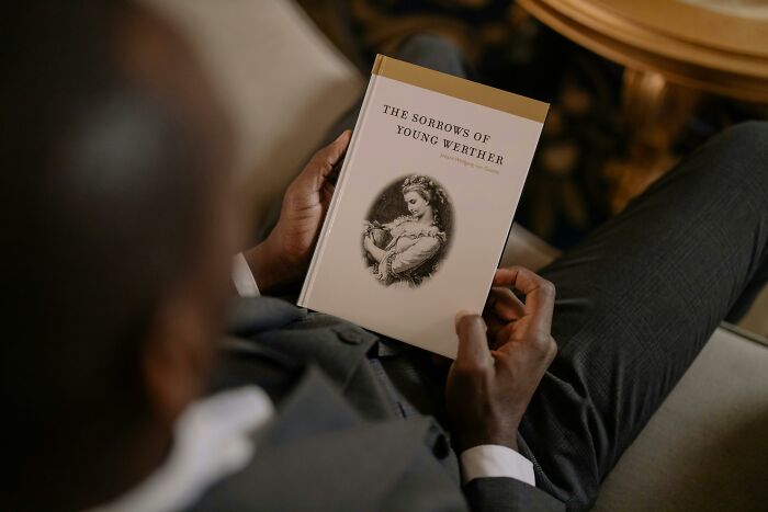 Man holding "The Sorrows of Young Werther," featuring a classic book cover in an elegant setting.