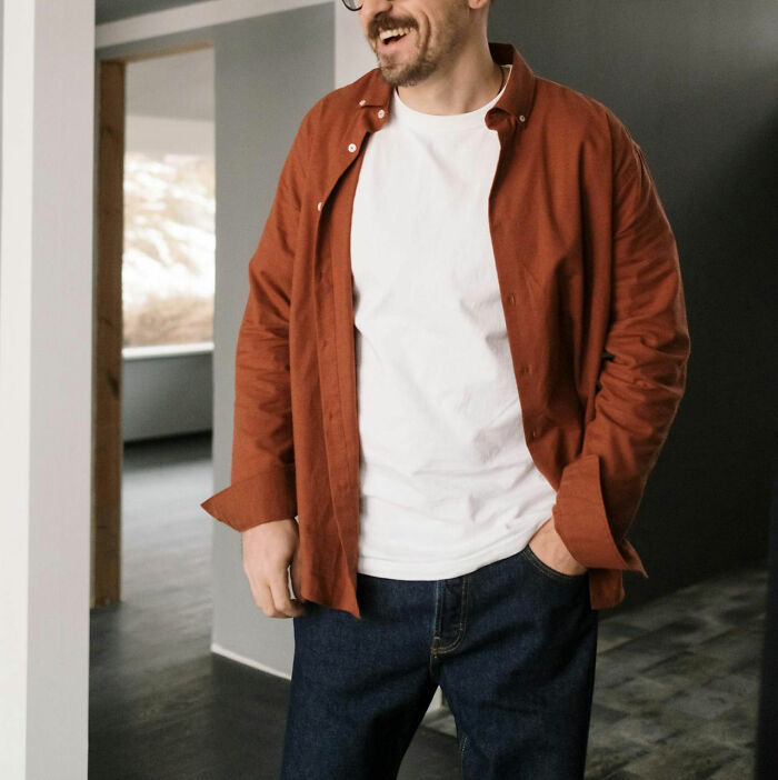 Man in casual attire, wearing a rust-colored shirt and white tee, standing indoors.