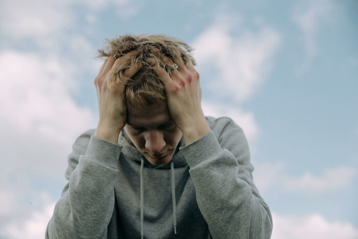 Person in a gray hoodie under a blue sky, holding their head, reflecting on a father's unforgettable words.