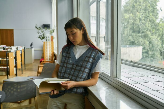 Person in a casual outfit reading by a window in a modern library, reflecting 2025 trends in lifestyle and design.
