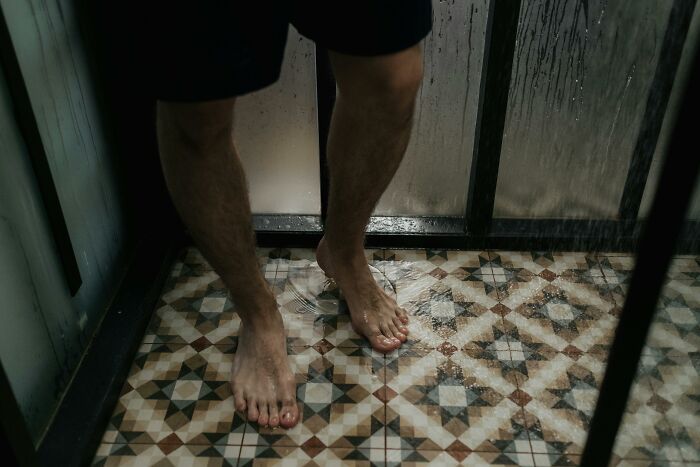 Person standing in a shower with patterned tiles, highlighting stereotypes about "real men."