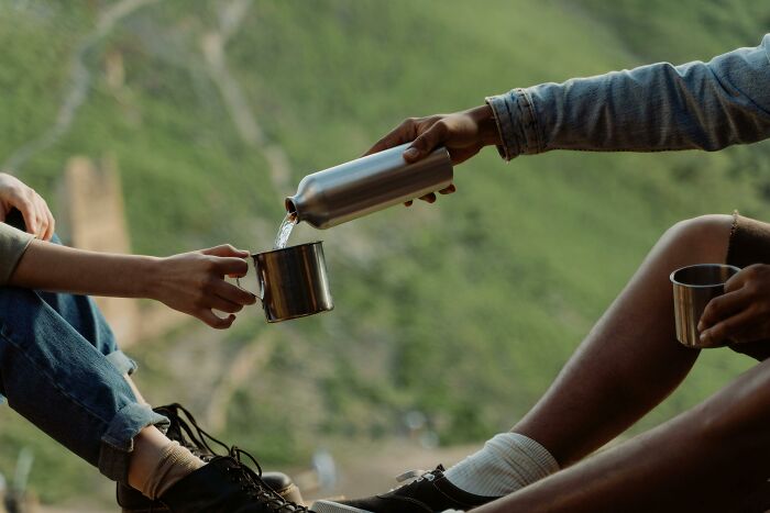 Two people pouring water into cups while sitting outdoors, illustrating self-paying-products concept.