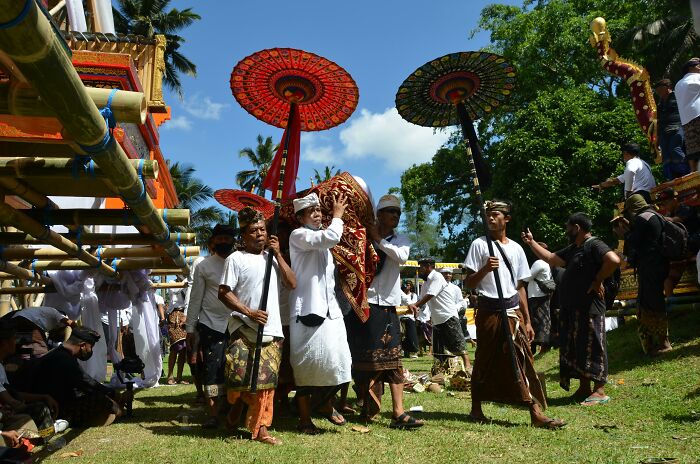 Cultural differences displayed in a traditional procession with vibrant umbrellas and ceremonial attire under a clear sky.