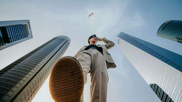 Person in a suit viewed from below, standing confidently among tall buildings with a plane overhead, capturing mic drop moments.