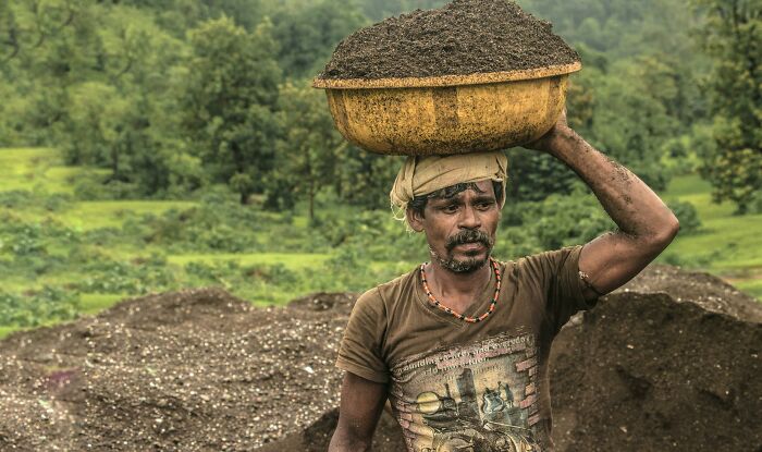 A man carrying a heavy basket of soil on his head, illustrating the hardest harsh realities about life.