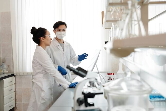 Scientists in a lab wearing white coats, masks, and gloves, discussing common job-related assumptions.