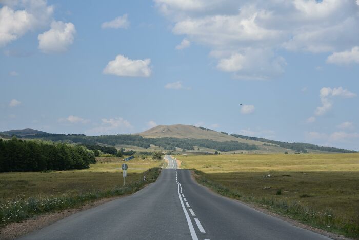 Open road through vast countryside under a blue sky, representing cultural differences in rural landscapes.