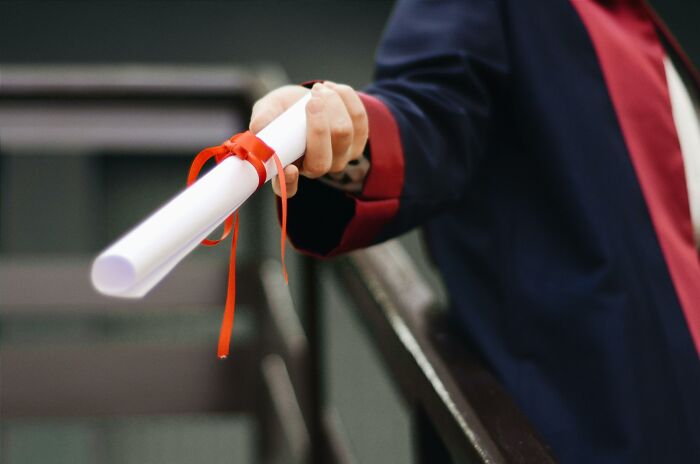 A hand in a suit holding a rolled-up document with a red ribbon, possibly during a conversation.