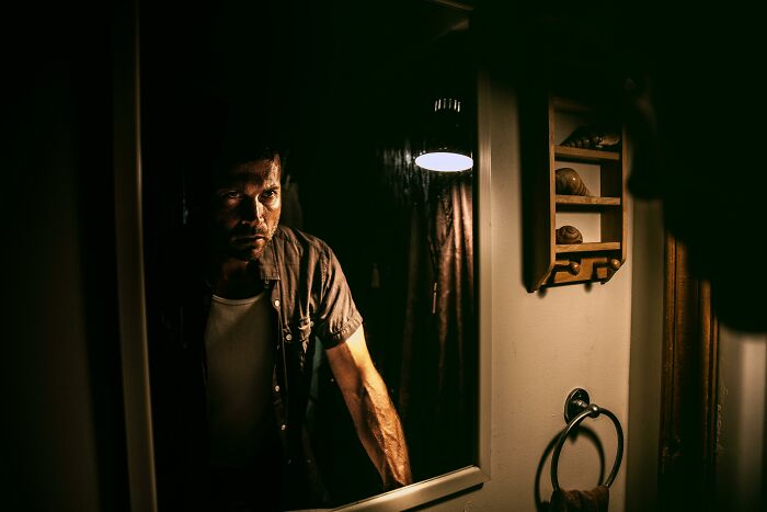 Man looking seriously into a bathroom mirror with low lighting, portraying themes of real men and self-reflection.