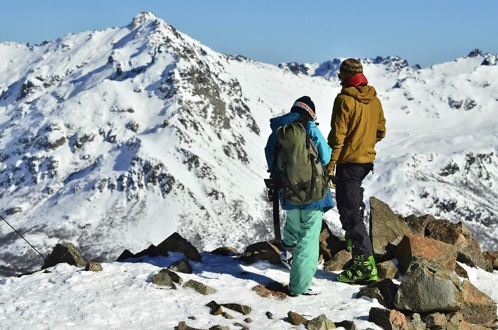 Two people in winter gear stand on a snowy mountain, possibly discussing self-paying-products.