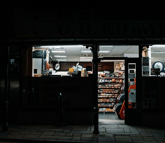 Night view of a small newsstand highlighting cultural differences in retail settings, displaying snacks and newspapers.