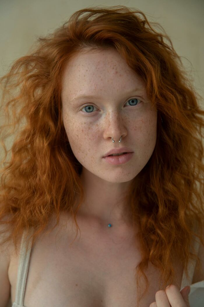 Person with a prominent nose and red hair, looking at the camera, showcasing unconventional beauty.