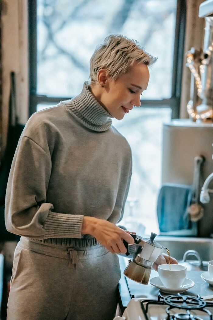 Person in cozy attire, preparing coffee at home, illustrating frugal living choices.
