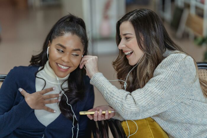 Two friends sharing earphones, smiling, highlighting ignored social rules.