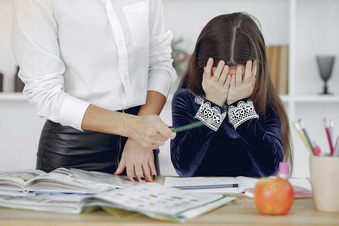 Child with head in hands at desk, adult pointing at a book; concept of life cheat codes.