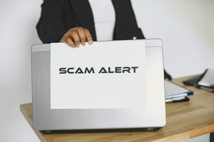 Person holding a "Scam Alert" sign over a laptop, highlighting work skills people lack in detecting online scams.