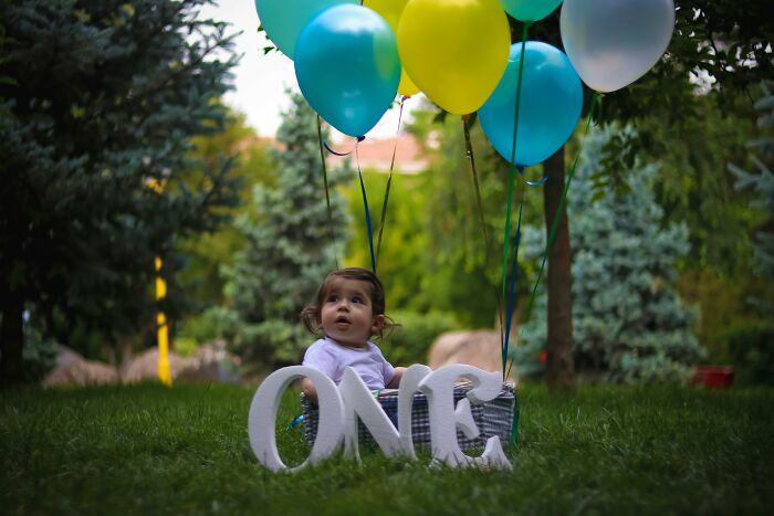 Child in a basket on grass with balloons and "ONE" sign, symbolizing change and growth related to therapists' knowledge.