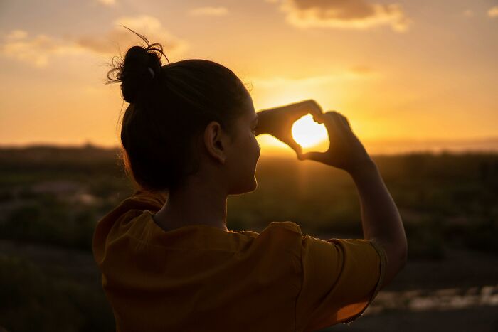 Woman making heart shape with hands at sunset, symbolizing things associated only with rich people and luxury lifestyle.