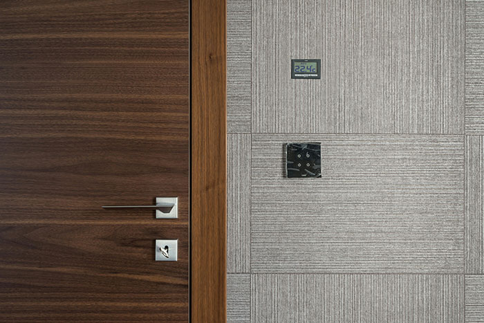 Modern wooden door with sleek handle and keyhole next to a wall with thermostat and control panel, representing perks of no office.