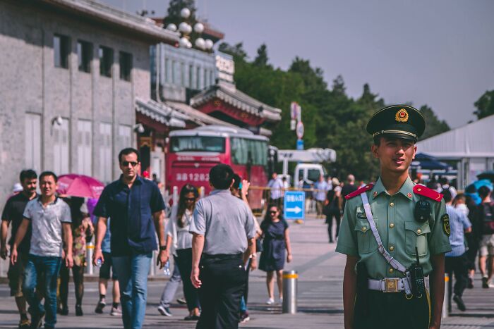Uniformed guard stands in busy street, showcasing cultural differences in public space.