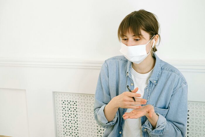 Person in a denim jacket wearing a mask and using hand sanitizer, related to weird government projects.