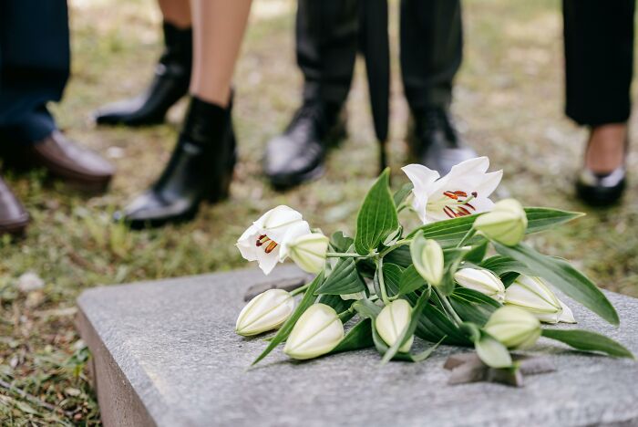 A bouquet of lilies on a gravestone, with people standing around, highlighting professions that provide essential help.